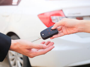 Close up of a person handing car keys over to another person in front of a white vehicle