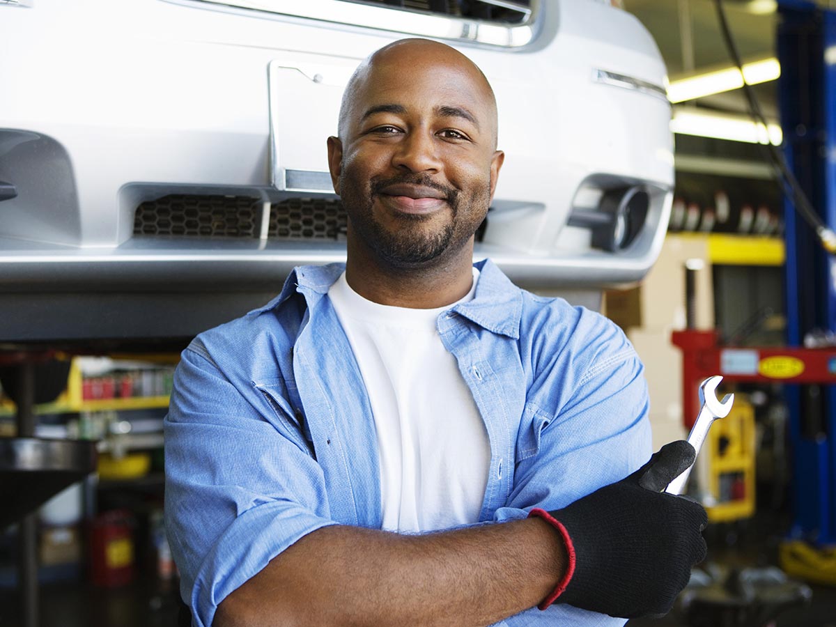 Smiling mechanic standing in front of a car in an auto shop